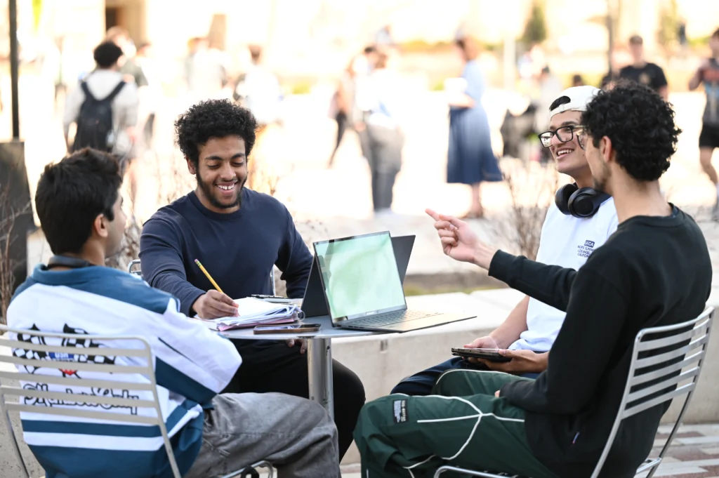A group of men sitting around a table working on their homework together outside in the sun