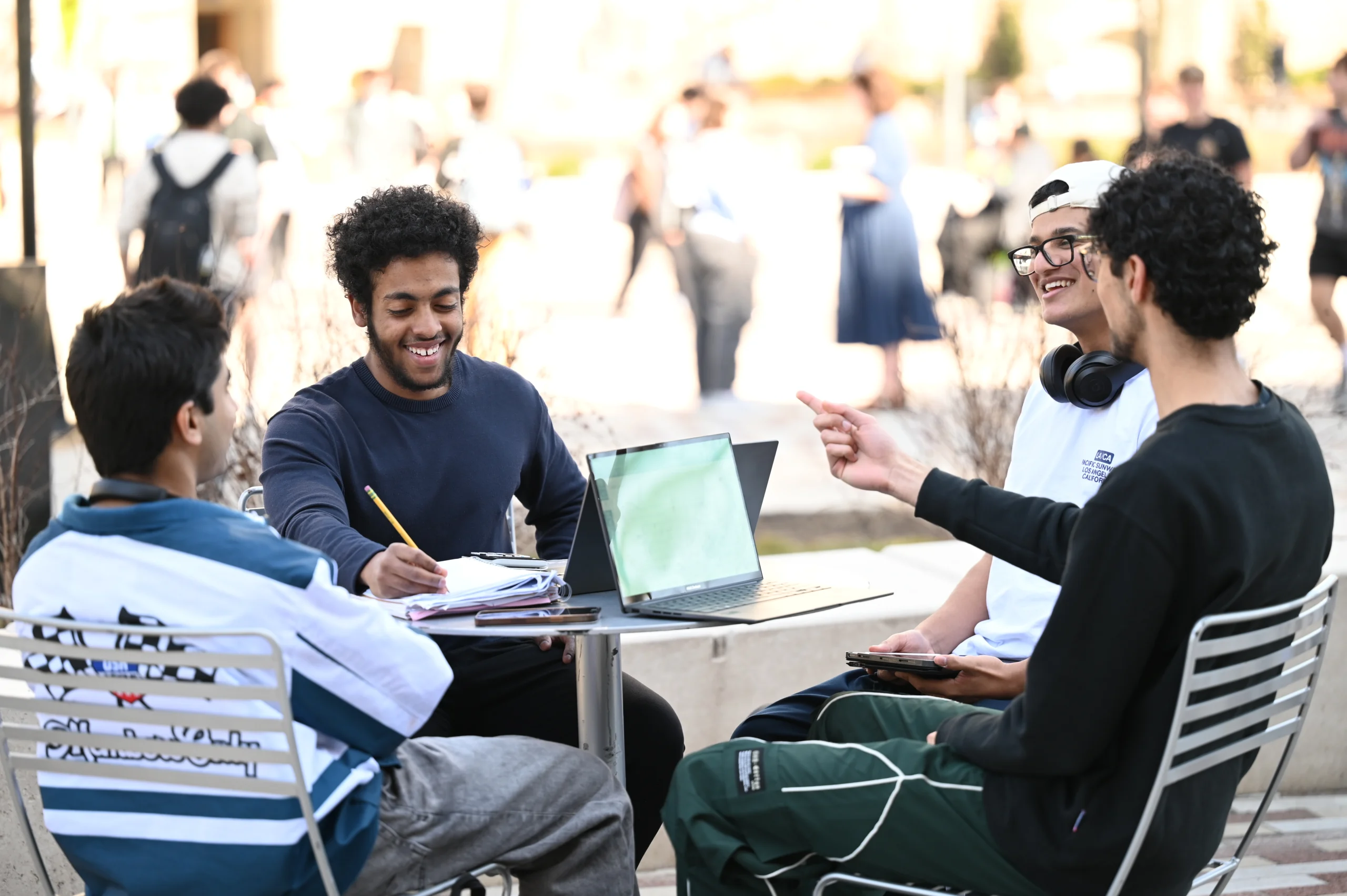A group of men sitting around a table working on their homework together outside in the sun