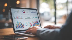 A person uses a laptop displaying various colorful data charts and graphs, analyzing metrics and statistics in a modern workspace.